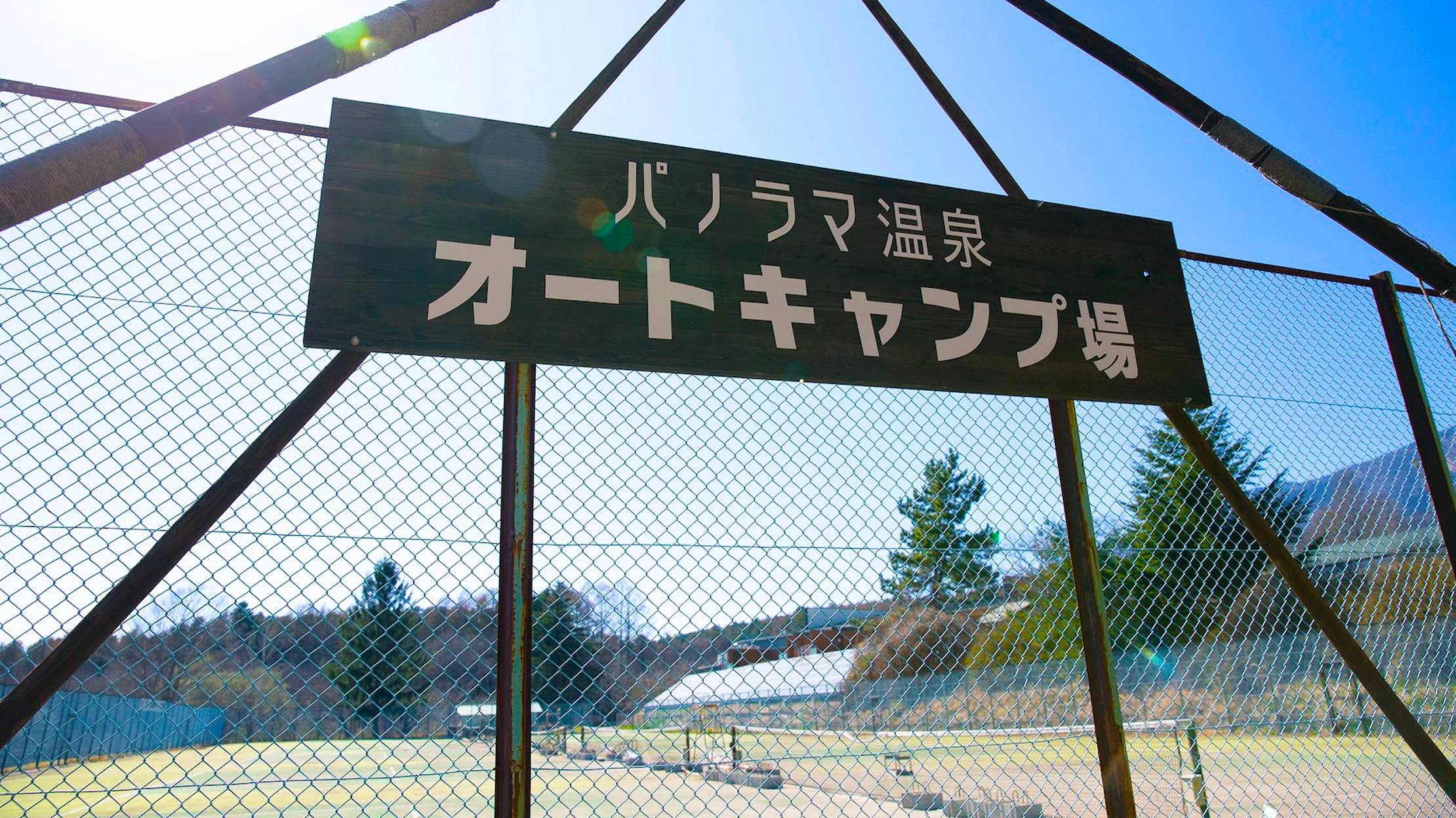 パノラマ温泉オートキャンプ場の入口看板とフェンス越しに見える場内風景