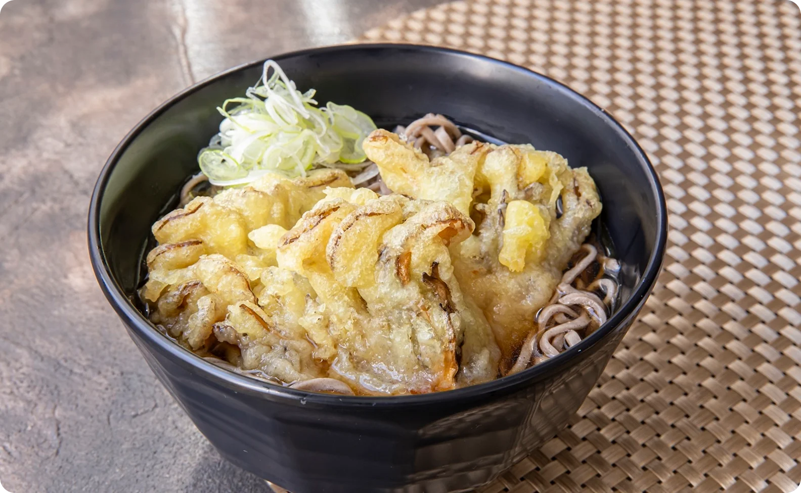 香ばしく揚がったきのこのかき揚げがのり、刻みネギが添えられた蕎麦（そば）のアップ