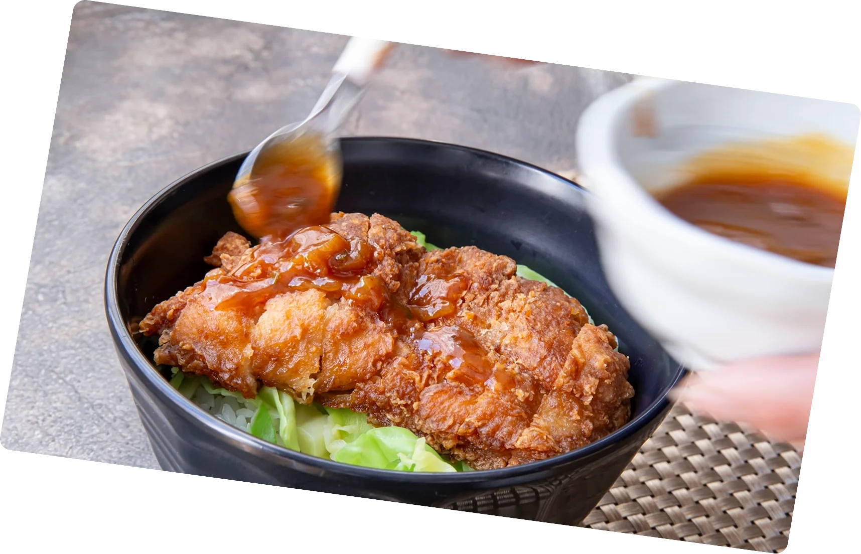 キャベツの上にカツがのり、特製ソースがかかるカツ丼を盛りつける様子