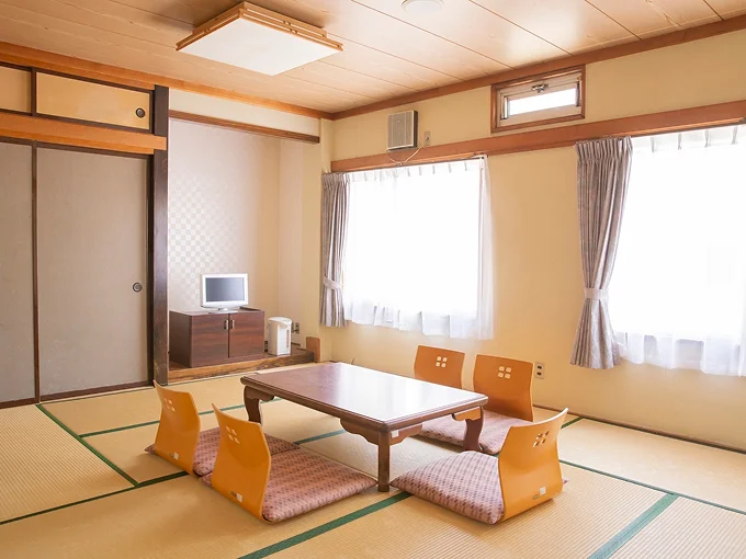 明るい和室10畳【禁煙】畳敷きに座卓と座布団、窓際にテレビやポットを備えたレトロな雰囲気のお部屋
