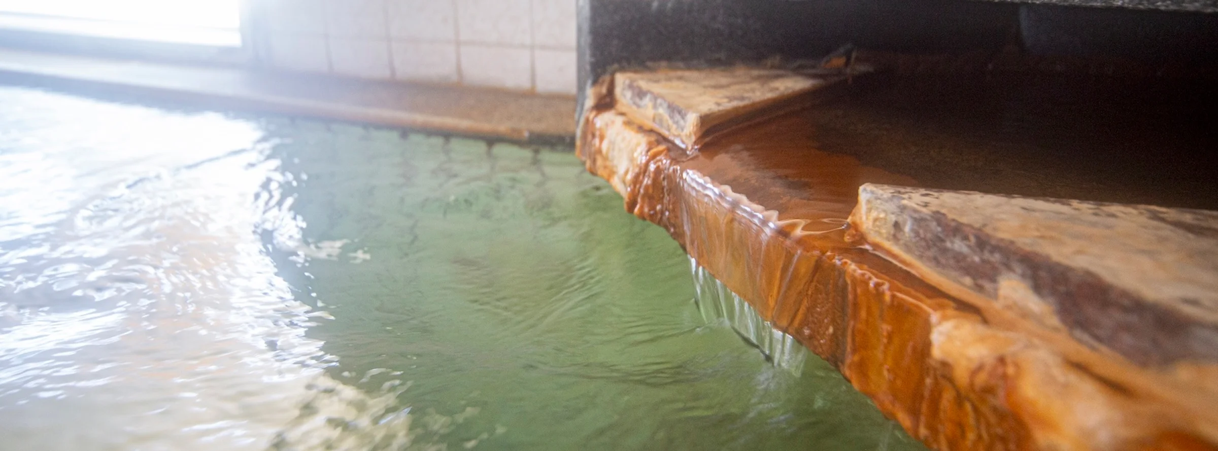 源泉から流れ出るお湯と析出物がついた縁のアップ（八ヶ岳いずみ荘 内湯）