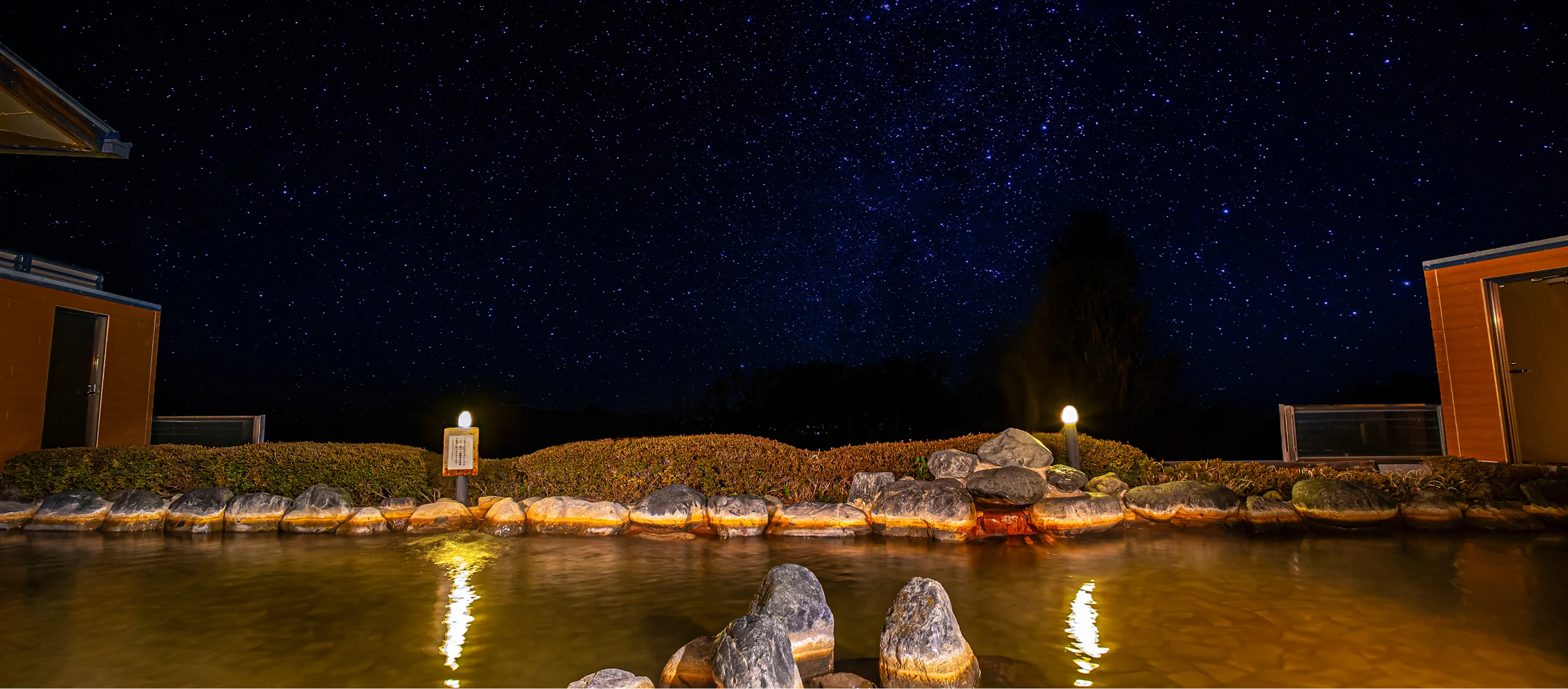 夜の露天風呂から眺める満天の星空と木々のシルエット